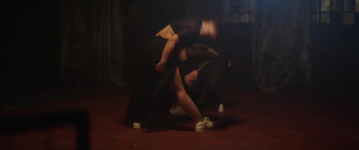 Two women dancing inside a dark room under a dim flickering spotlight