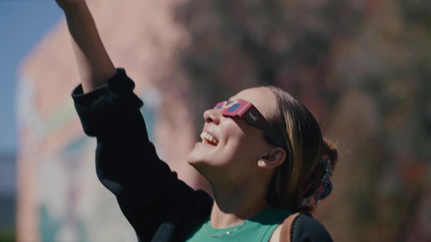A woman with protective sunglasses smiles and points to the sky