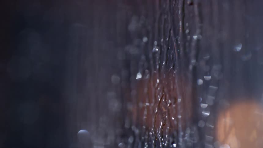 Rain water running down a window at night time