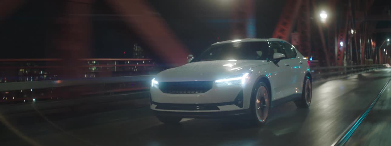 White car traveling over a bridge and in the background a metropolis with skyscrapers illuminated at night