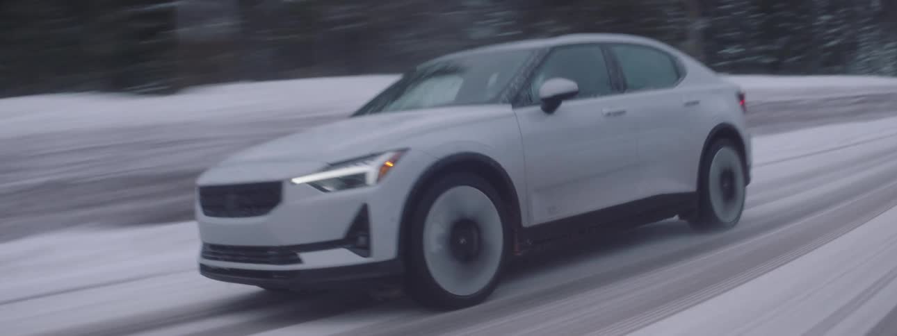 A white car driving on a snowy road next to a pine tree forest