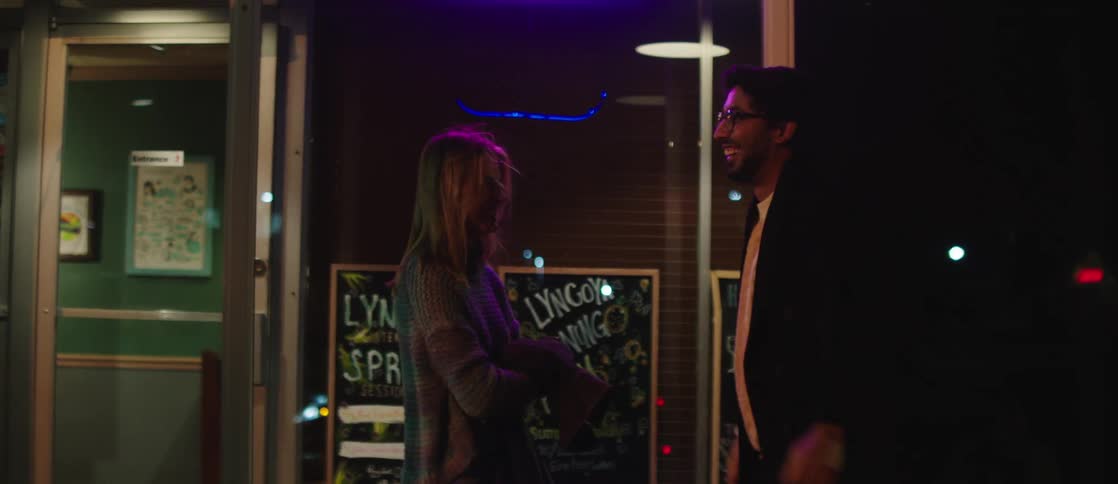 A young happy couple walk out of a restaurant in the city at night