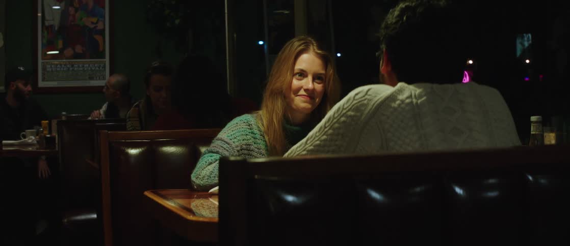 A couple sits together in a busy restaurant talking a waitress brings them their bill the women smiles and laughs