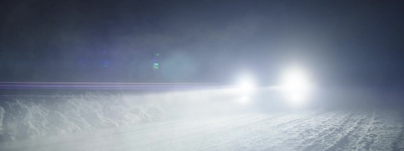 Car with headlights on driving along a snowcovered road at night