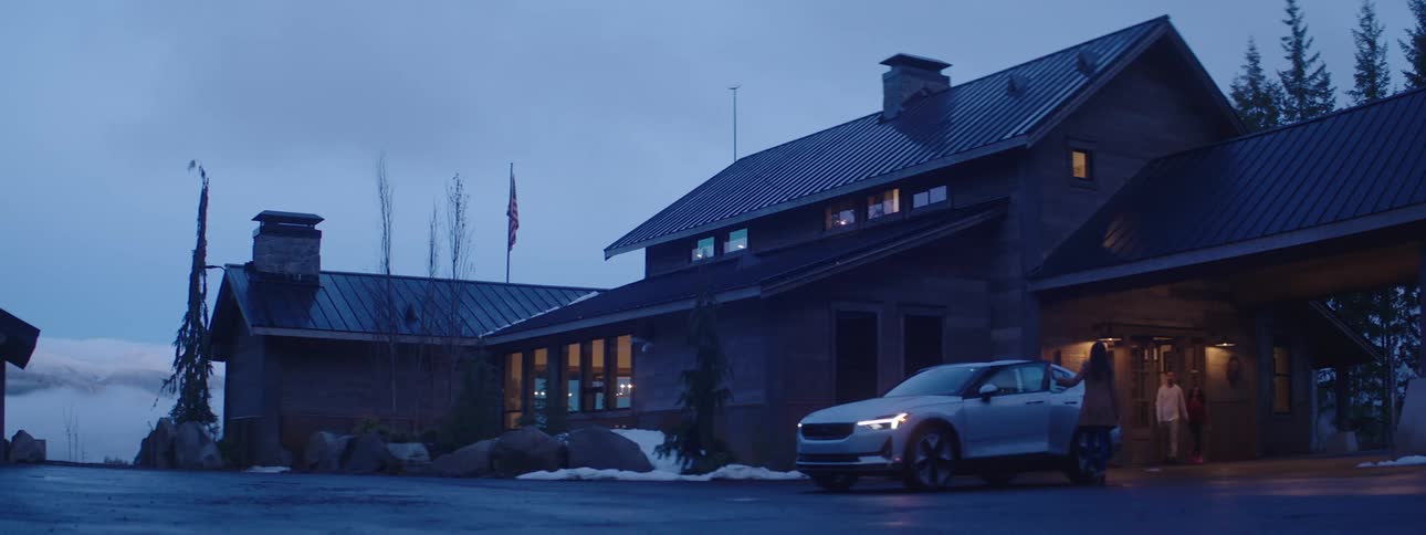 People exit residential building to greet woman arriving in car after dusk during winter