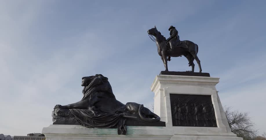 Bronze monument of a person on horseback and a lion in a square on a blue sky day