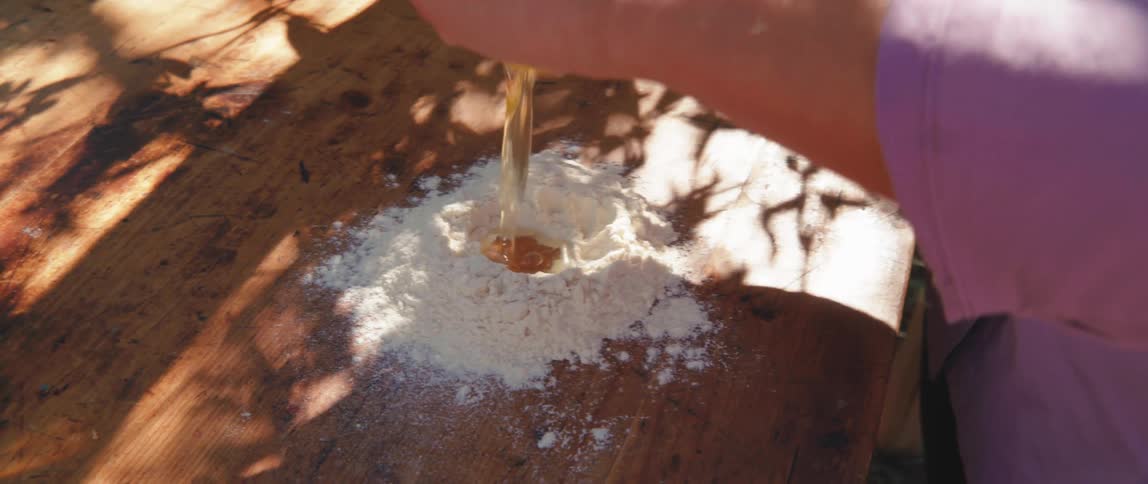 Woman hands breaking an egg into flour on a wooden table outdoors