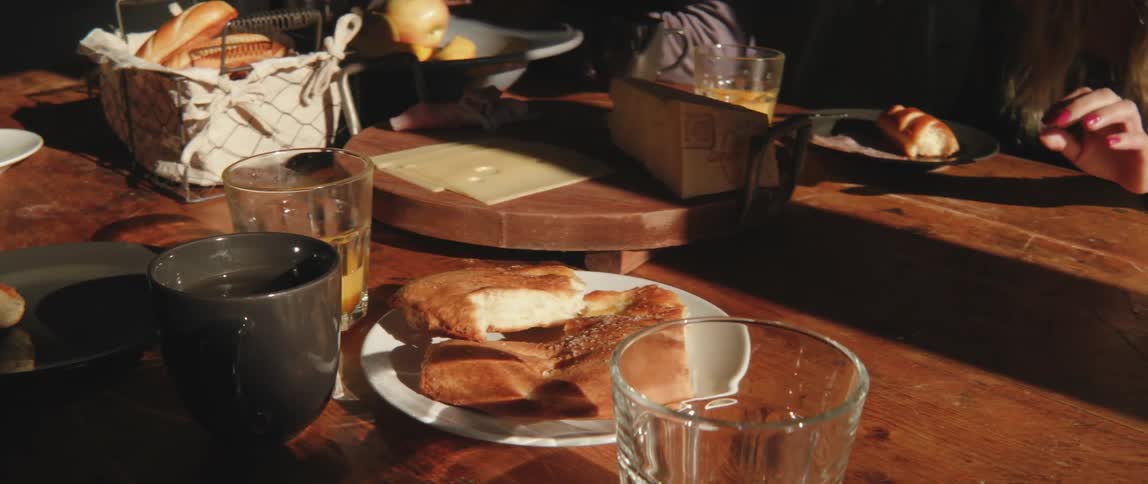 Wooden table with cups glasses and bread and a womans hand picking up food