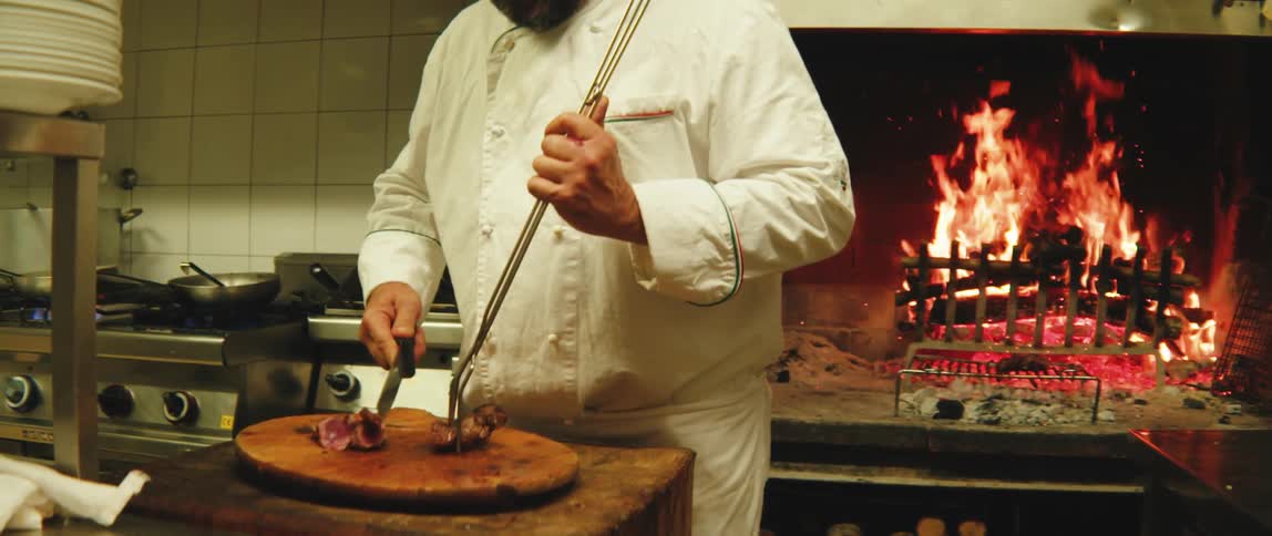 A chef cuts meat on a wooden cutting board