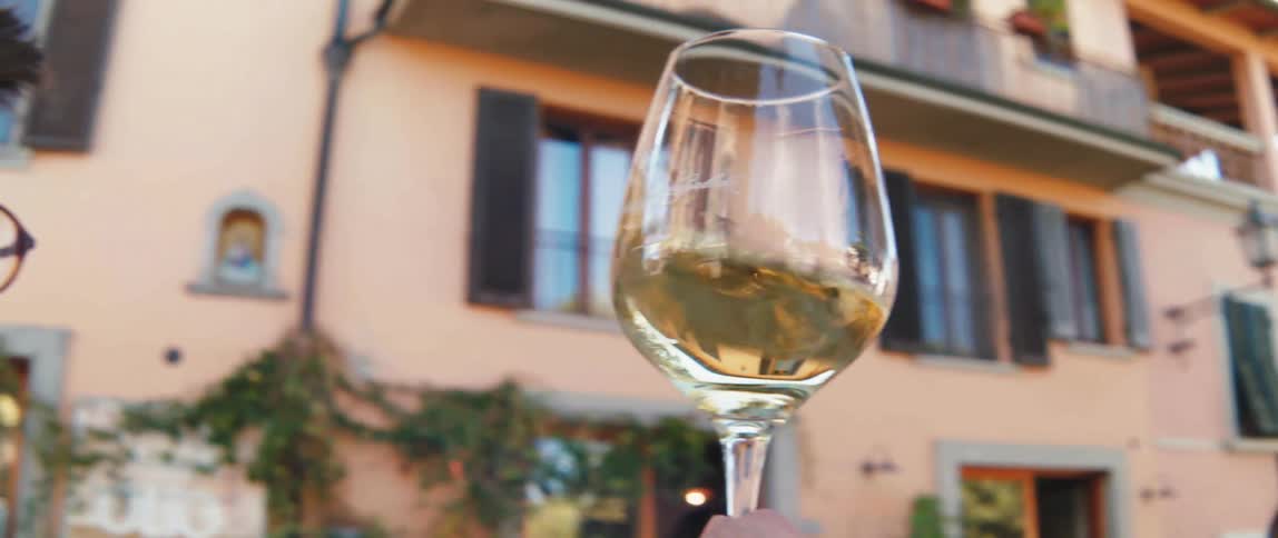 A closeup of a hand holding a glass of white wine with a building in the background