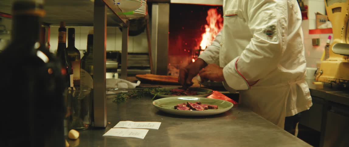 A chef in a white uniform working near an open flame in a kitchen
