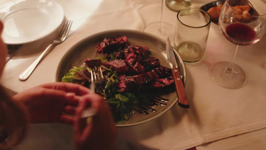 Woman sitting at the table eating a plate of vegetables and roast meat