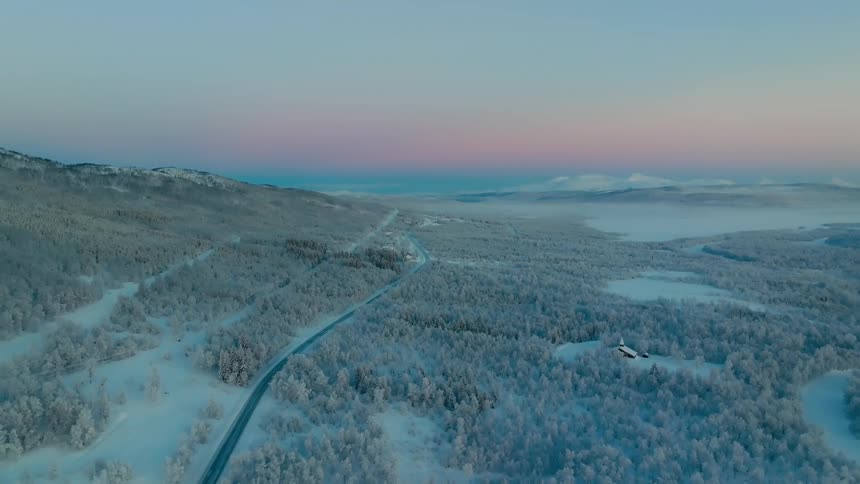 Aerial view of a road through icecovered mountains under a pinkish sunrise sky