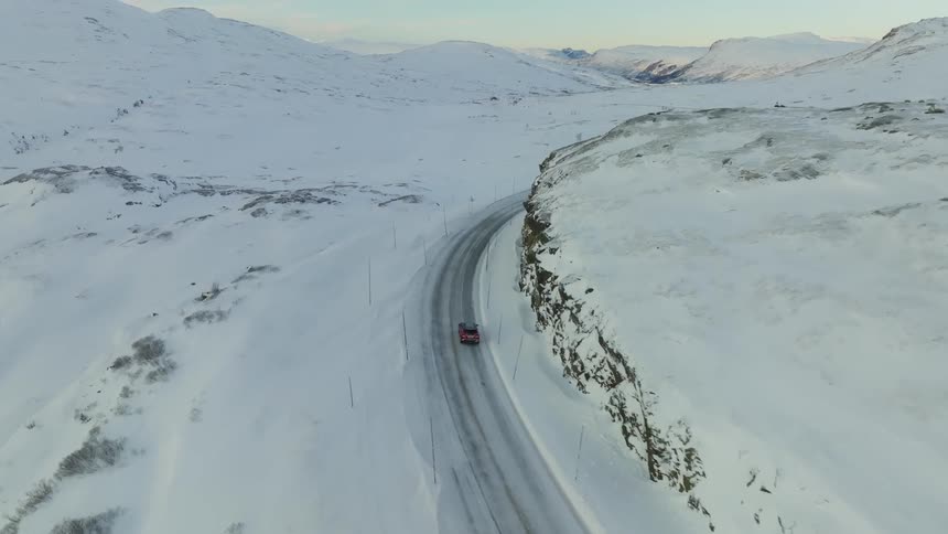 Aerial view of cars driving on a remote road through a snowy landscape