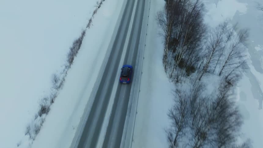 Cars drive on a road next to a river in a snowy landscape