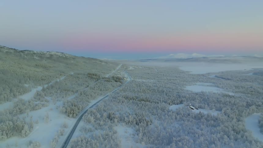 Aerial view of a small road winding through a forest completely covered in snow