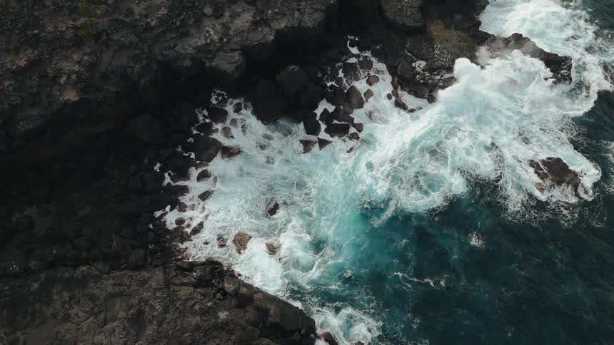 Aerial landscape of a turquoise sea with waves crashing on the rocky shore