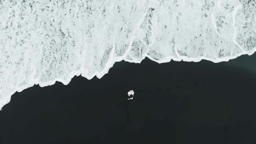 A woman wearing a white dress walks along the ocean shore