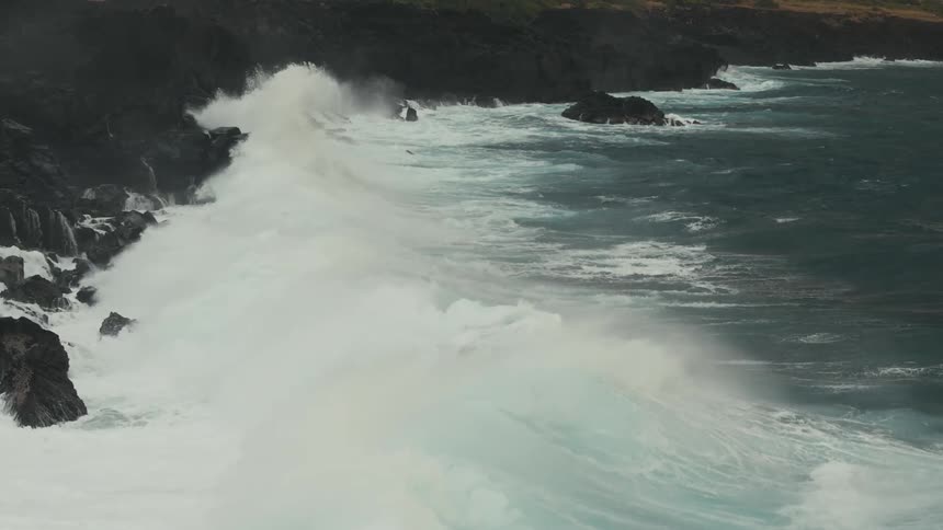 Waves crash on the rocks at the base of a cliff at the shore