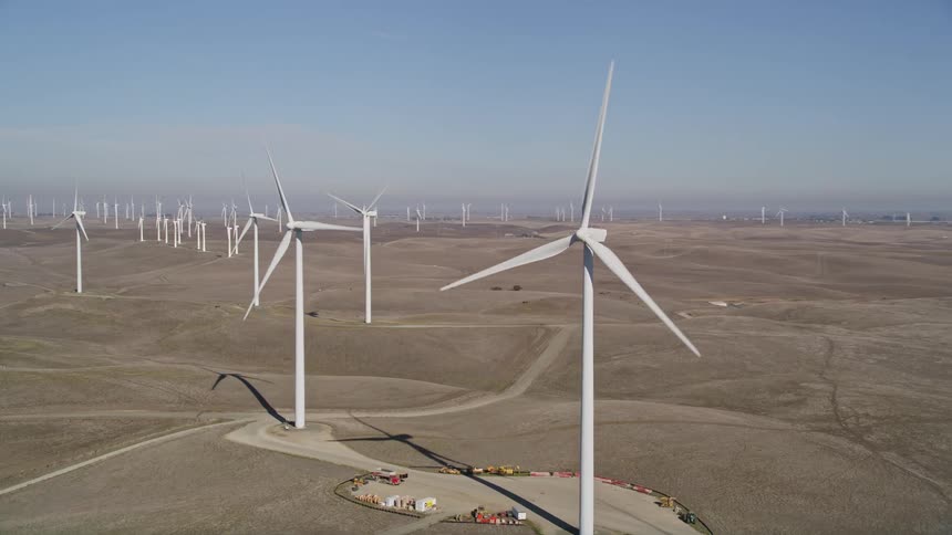 Panorama of wind energy towers and engines moving across extensive fields during the day
