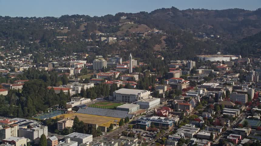 An aerial view gave a city that has a large white tower and there are many trees and a hill behind