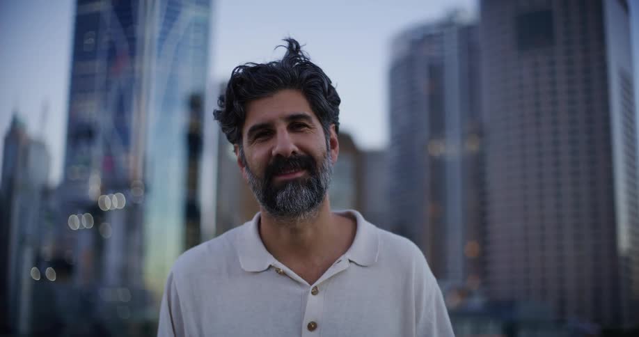 A man stands and smiles against the backdrop of a city