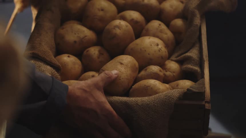 Close up of a person placing a crate of potatoes over a counter