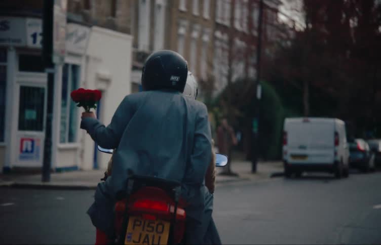 A person holding flowers rides on a motorcycle through a city