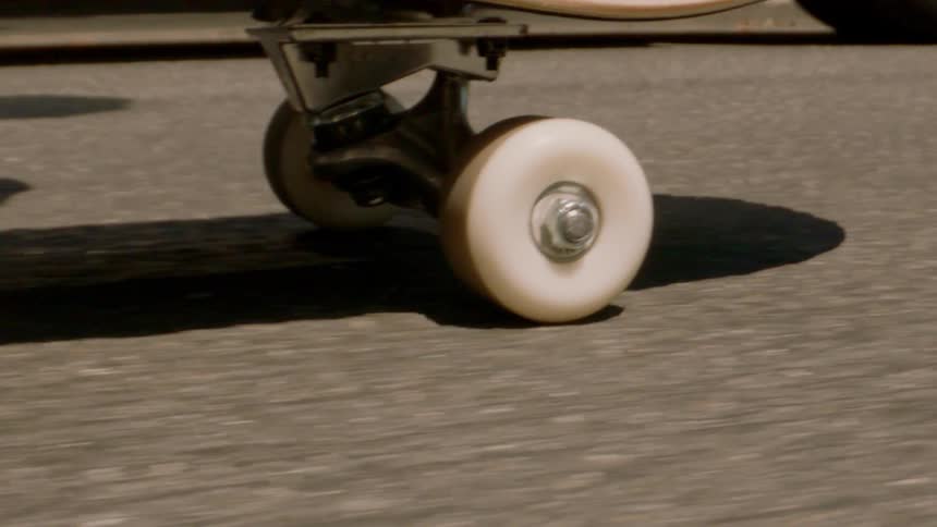 Closeup of a skateboard with a person riding on the asphalt
