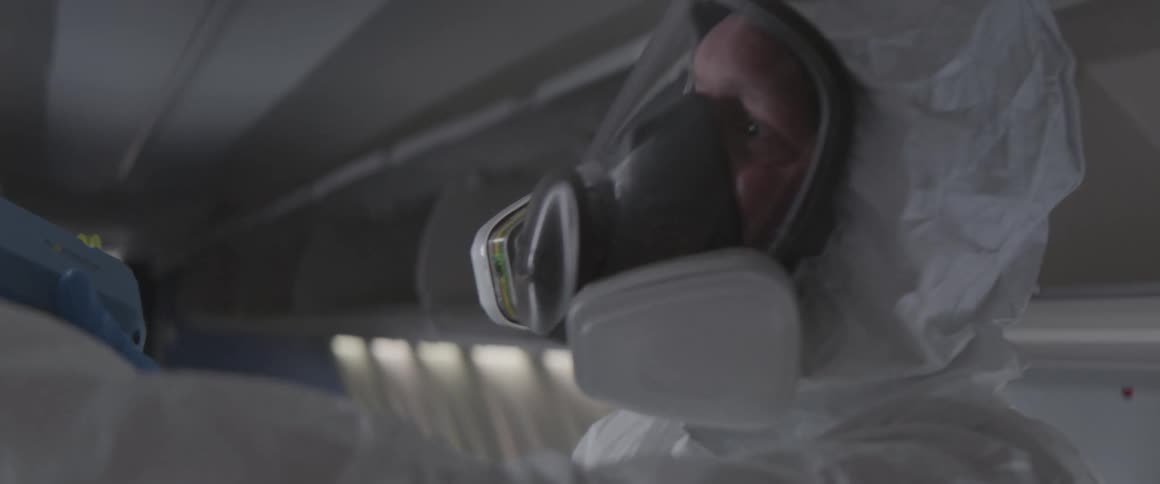 A man with a gas mask and white clothes is cleaning something in front of him