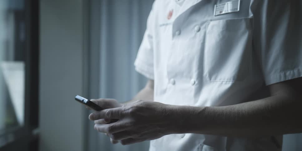 Man wearing a work uniform texts on his smartphone before pocketing it