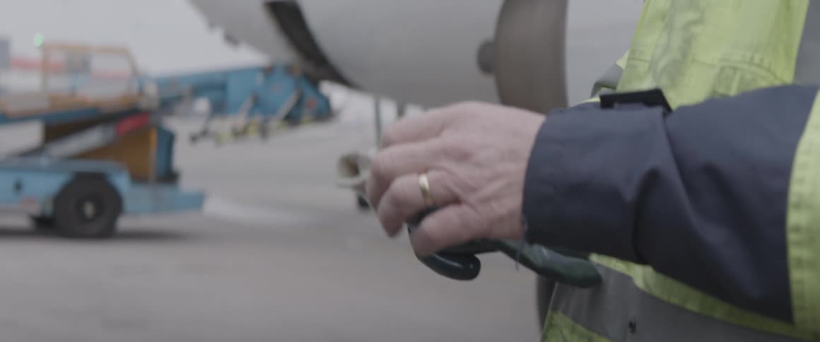 Closeup of a mans hands putting on gloves next to an airplane