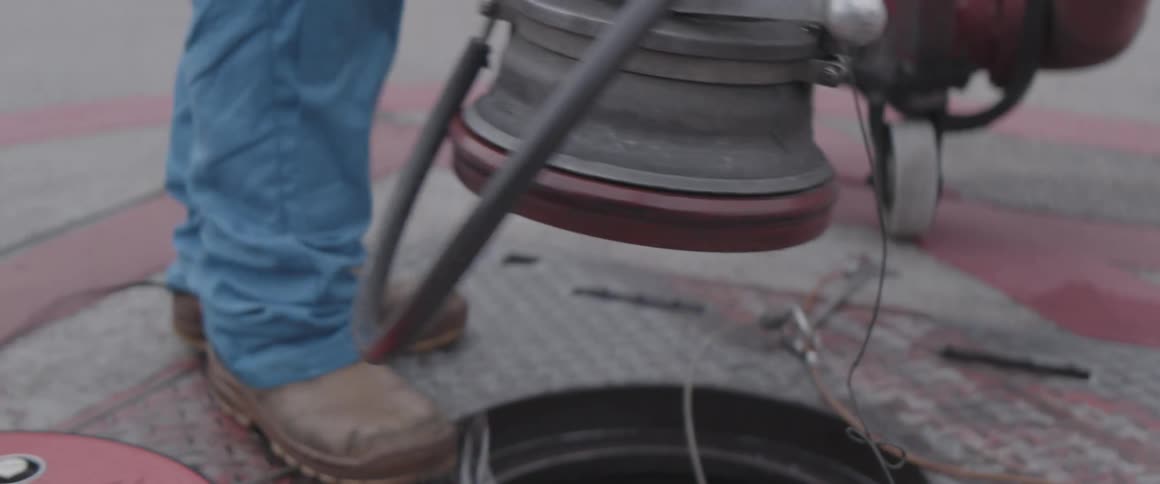 A person in blue gloves handling a metallic device above an open manhole