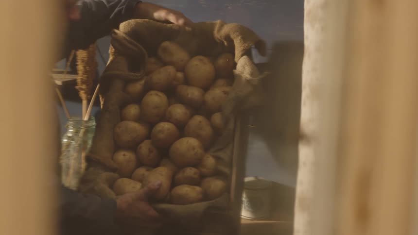 A person carrying a crate of potatoes into a rural kitchen