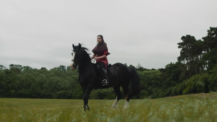 A medieval woman is riding her horse on the grass
