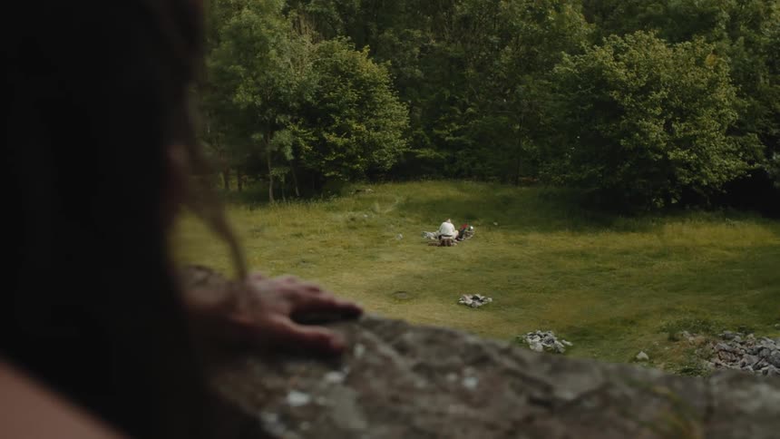 A man on a building looks at a person sitting in a field