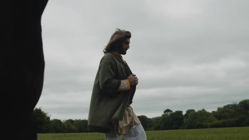 Man walking next to a horse in an open forest on a cloudy day