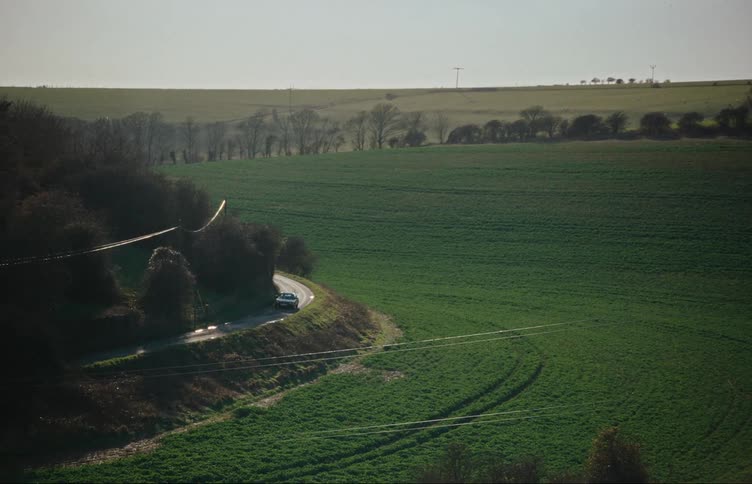 Aerial panorama of a vintage car traveling down a narrow street on the edge of a rural area