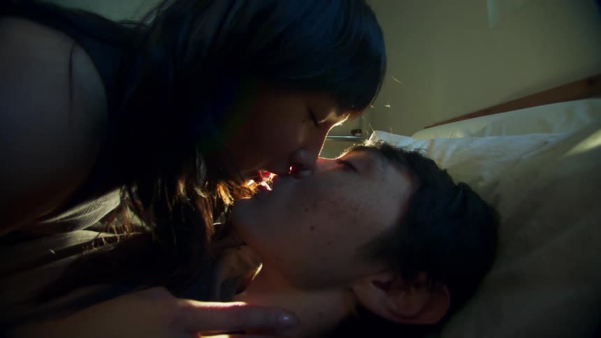 Couple lying on bed kisses while light briefly creates red glare
