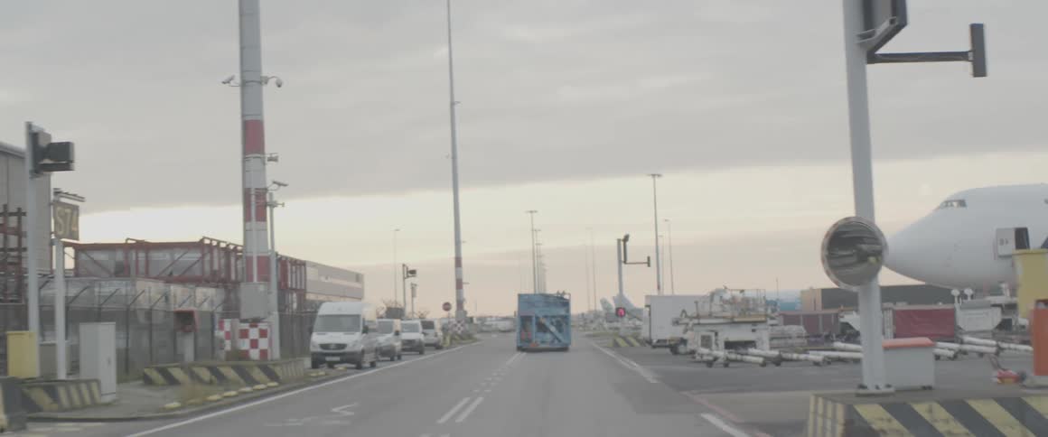 Blue gasoline truck driving on an airport road with planes and cargo around