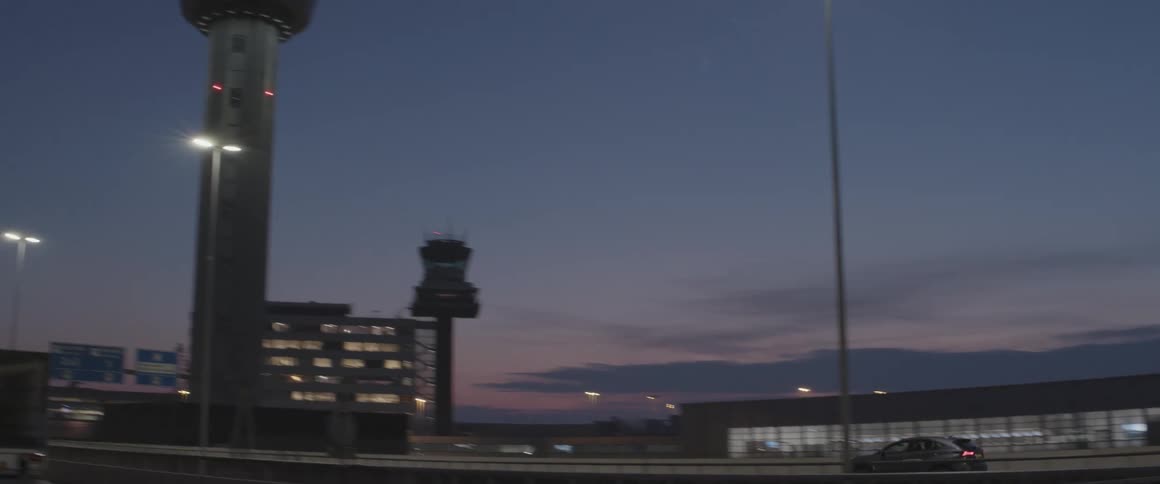 Car passing on an airport runway with a conning tower next to it in night vision