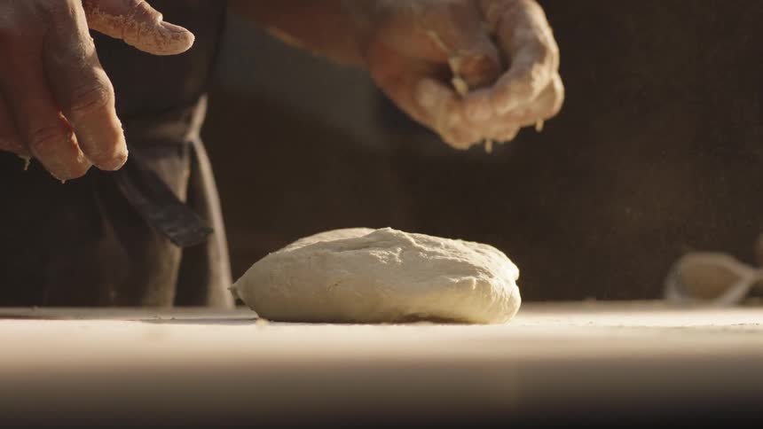 A mans hands throwing fresh bread dough onto a surface