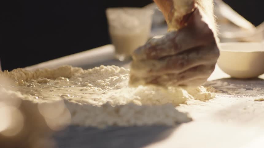 A closeup view of a doughcovered surface with a persons hand kneading the dough