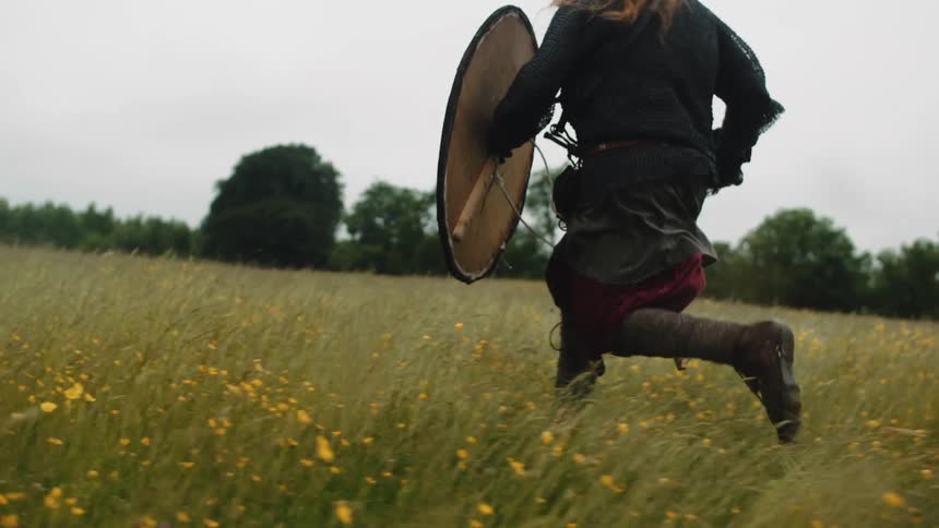 A warrior holding a shield is running through a field