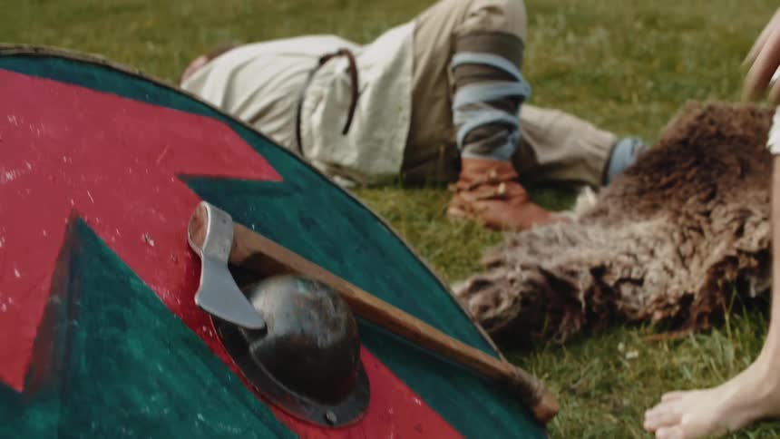 A man grabs an ax leaning against a shield