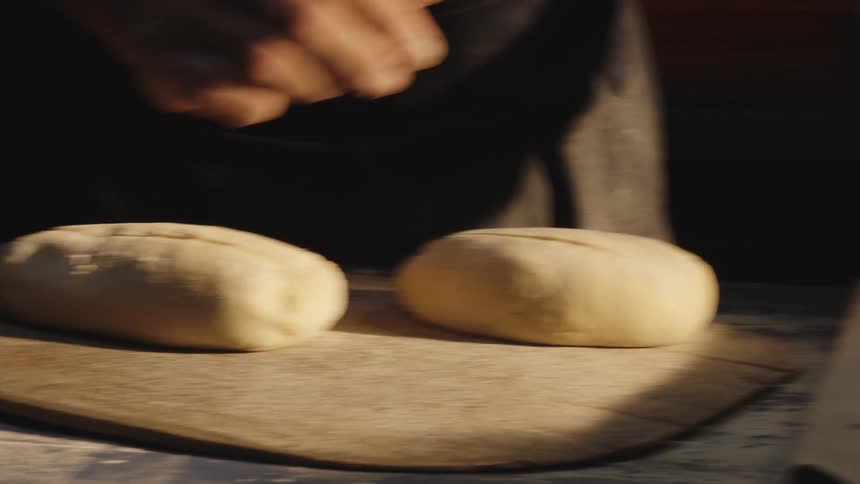 Mans hands placing bread dough on a wooden board and making a cut in the top of the dough