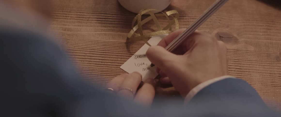 A person writes a note on a tag and attaches it to a gift
