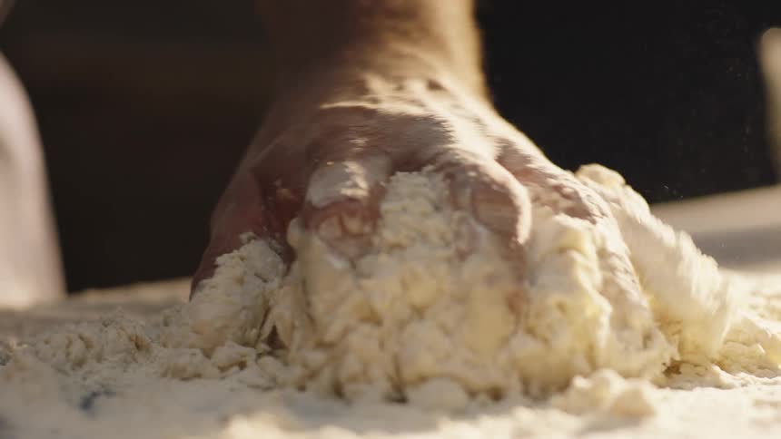 Male baker mixes dough on floured surface