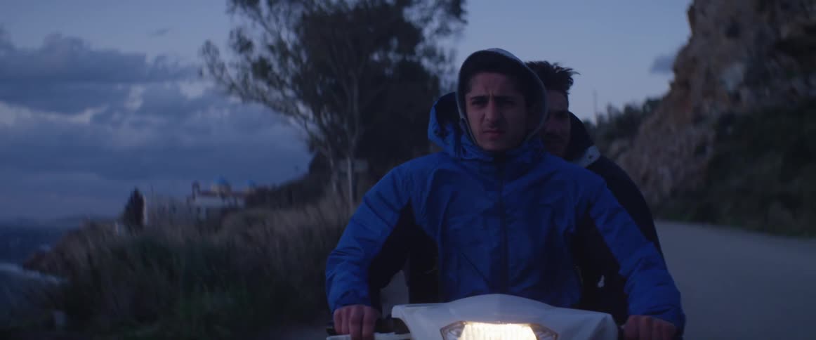 Two men ride a motorbike at dusk