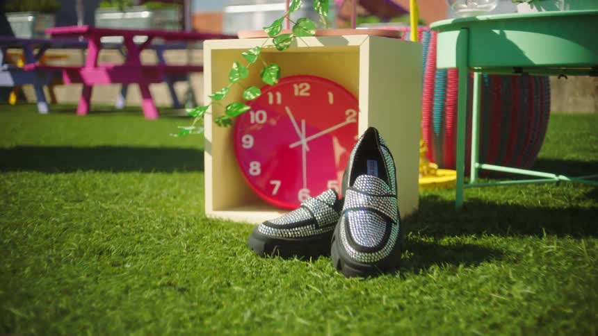 Boot with shiny sequins next to a watch in a box on the ground in the grass